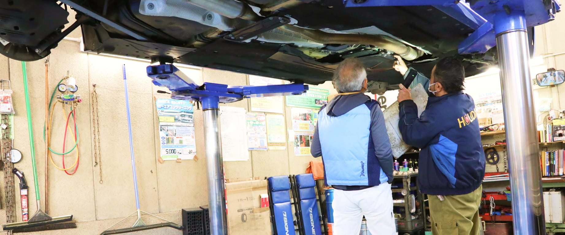 自動車の下部を点検している整備士が工場内で作業している様子の写真